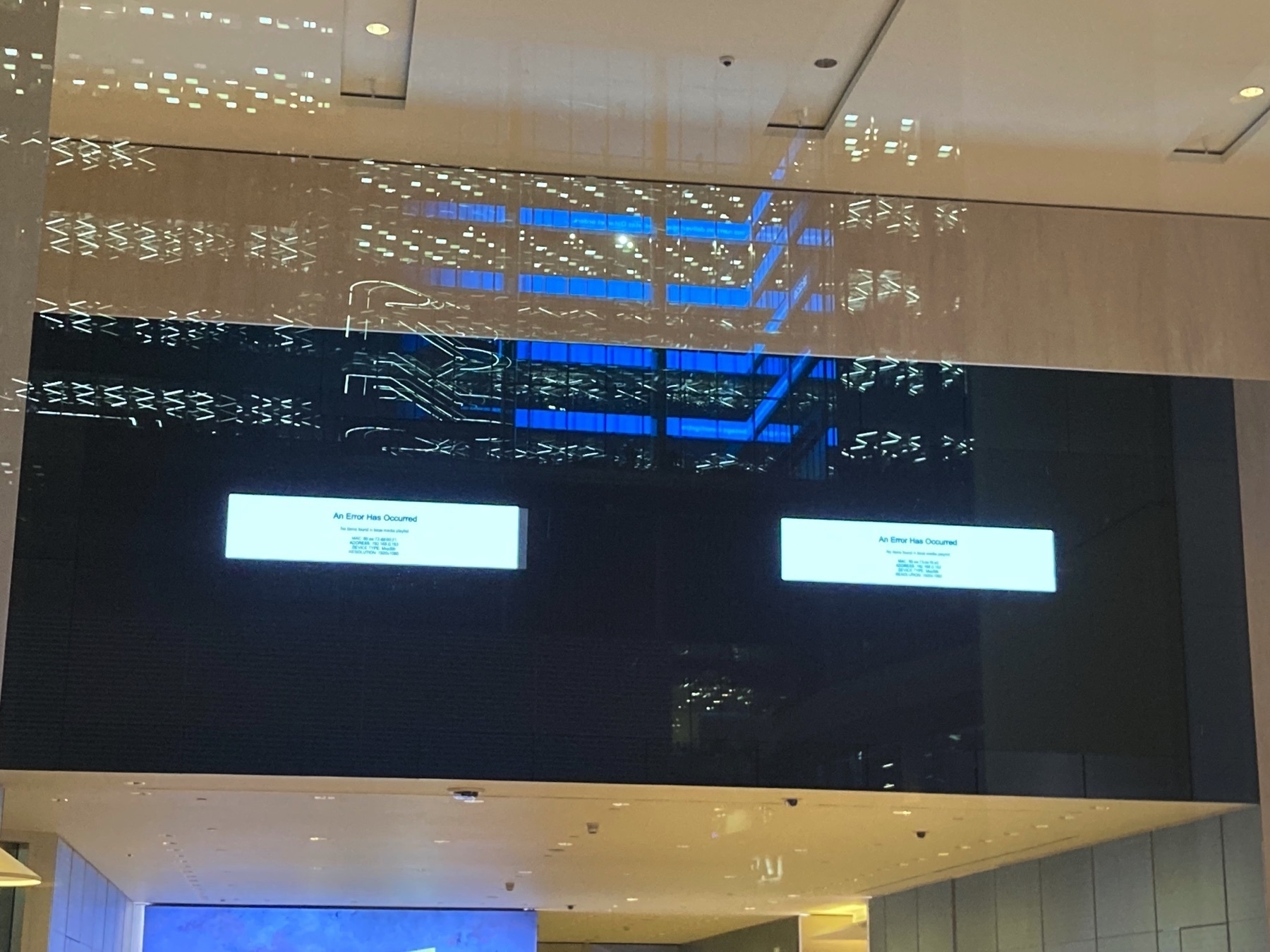 Looking through a window full of reflections at a large digital signage screen that has crashed at EY, Canary Wharf.